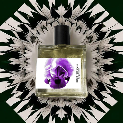 A perfume bottle with a black cap is centered against an artistic background. The label reads "Rook Perfumes London | Unique Unisex Fragrance" and features a purple and black floral design inspired by the Faqqua Iris, the national flower of Palestine. The background consists of black and white abstract patterns resembling petals radiating outward.